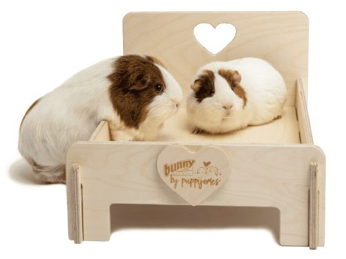 To gnavere sidder på en træbed med hjerteformet udsnit, designet af Bunny by Puppijames. Bedet tilbyder komfort til marsvin og mindre kæledyr.